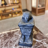 Close-up detail of crossed arms on black cube block statue, museum reproduction