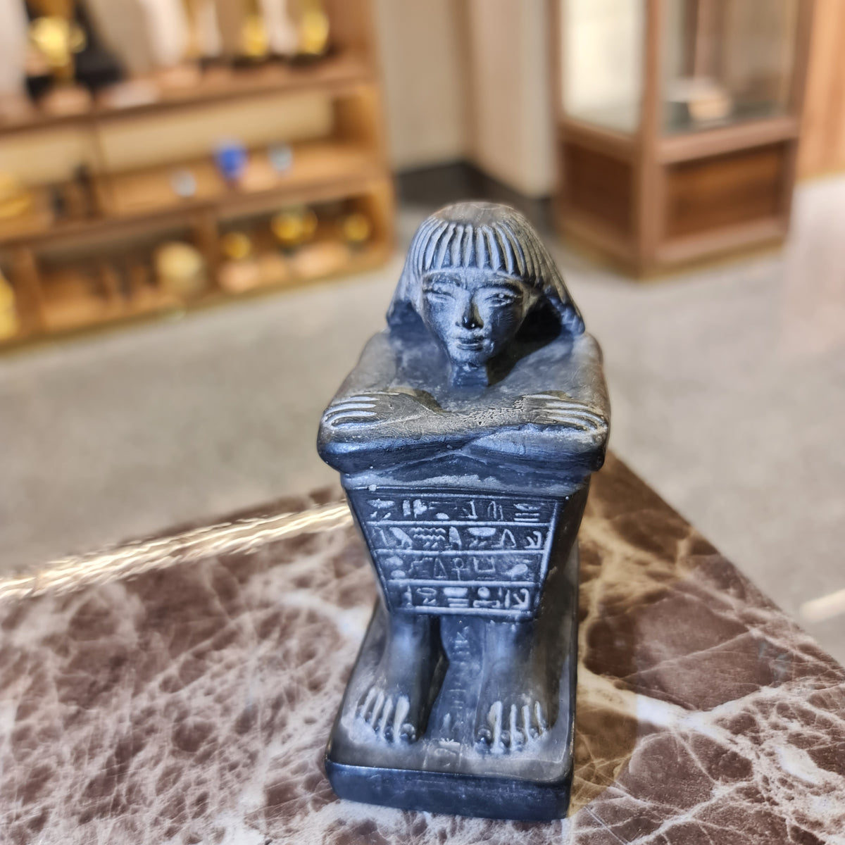 Close-up detail of crossed arms on black cube block statue, museum reproduction